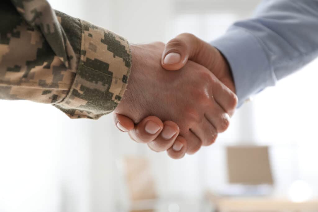 Soldier and lawmaker shaking hands indoors, closeup