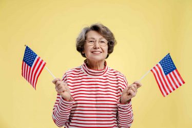 Portrait of attractive senior American woman holding American flag, patriot wearing casual sweater